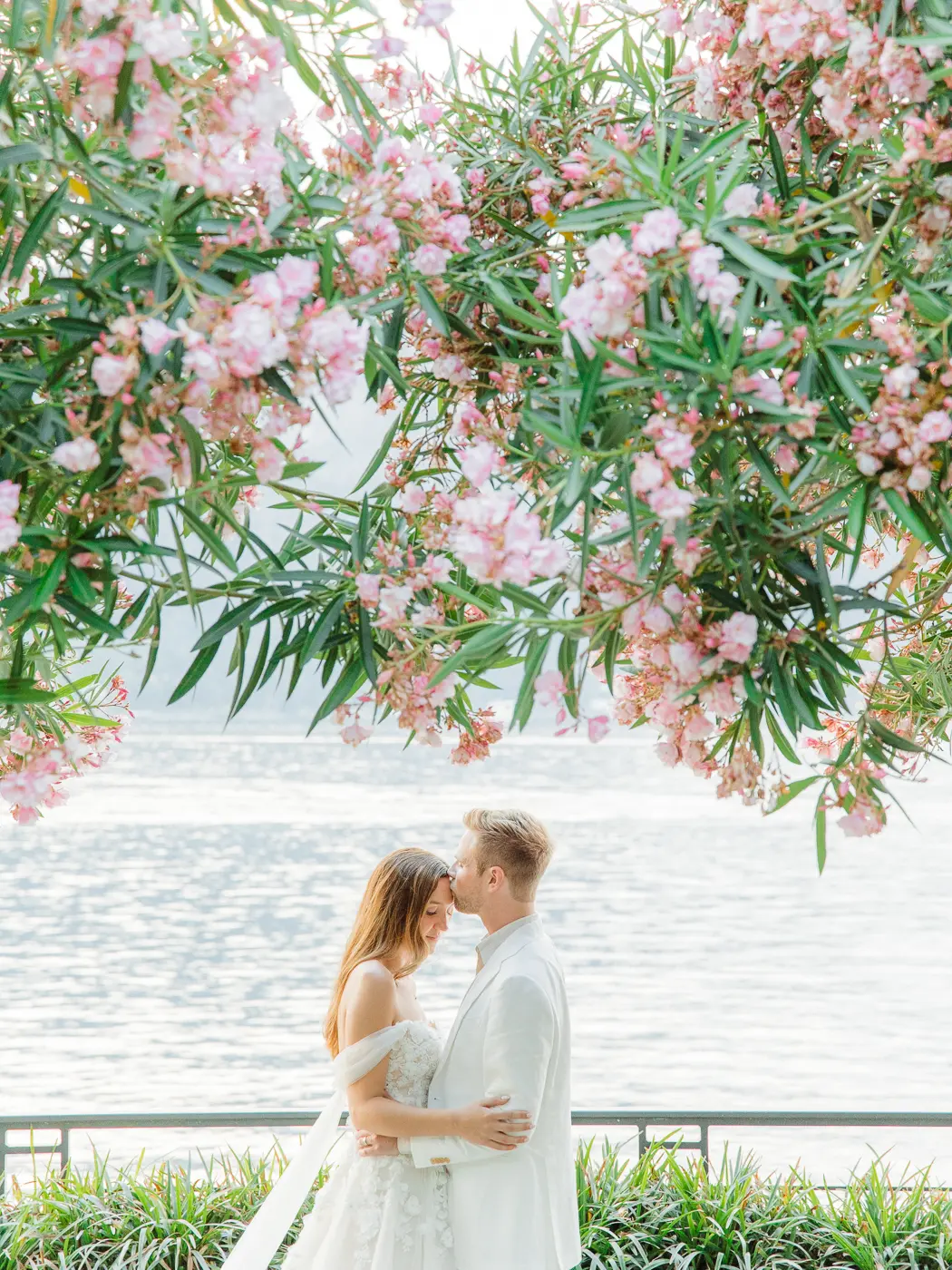 A candid moment captured as the newlyweds share a kiss against the enchanting backdrop of Lake Como's azure waters and booming fowers