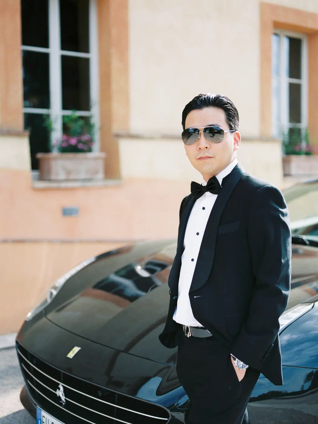 Stylish portrait of the groom with ferrari car in front of the historic stone walls of a medieval villa